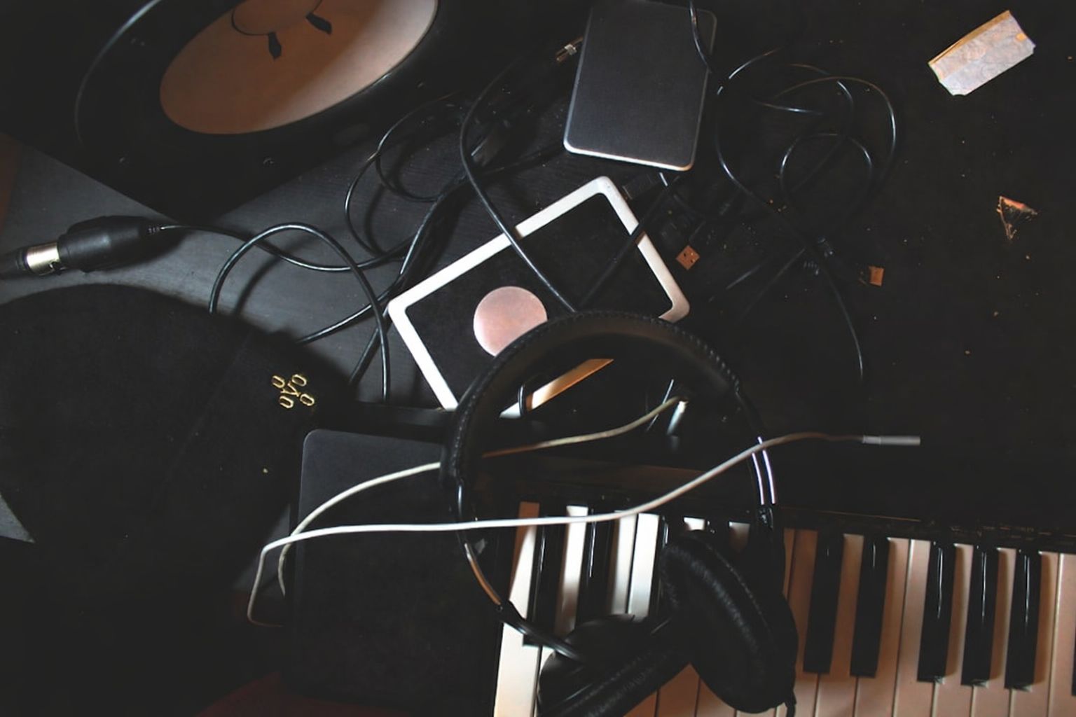 Mörk bild med musikstudio-utrustning, inklusive hörlurar, keyboard och kablar.