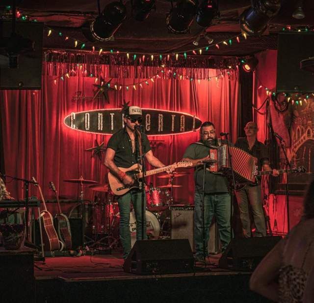Ett band uppträder live på scenen på Continental Club i Austin under röda ljus.